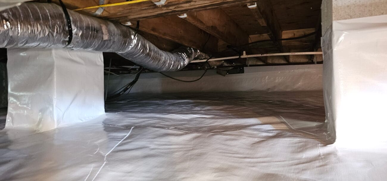 A crawl space with exposed wooden beams and ductwork, lined with white plastic sheeting on the floor and walls.